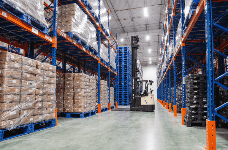 Automated cold chain logistics warehouse with high-density racking systems storing palletized goods on blue plastic pallets. A warehouse forklift operates in the central aisle, supporting warehouse automation in a temperature-controlled environment.
