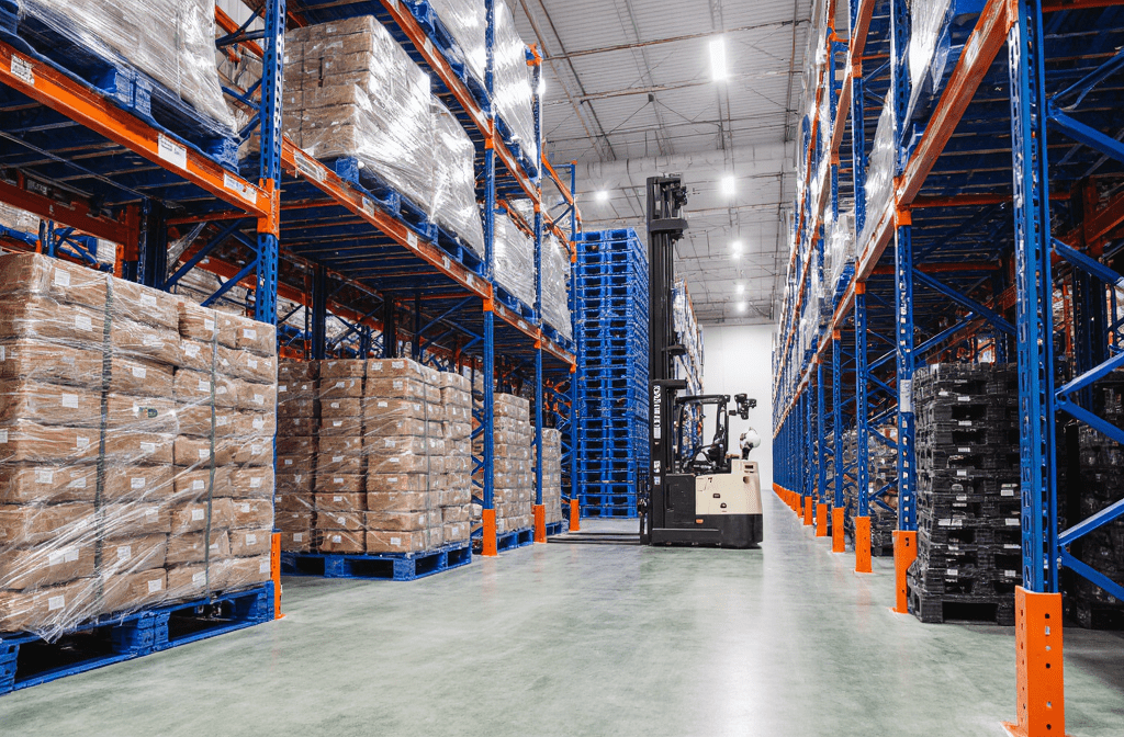 Automated cold chain logistics warehouse with high-density racking systems storing palletized goods on blue plastic pallets. A warehouse forklift operates in the central aisle, supporting warehouse automation in a temperature-controlled environment.